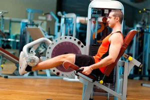 Homem jovem em uma cadeira flexora de academia